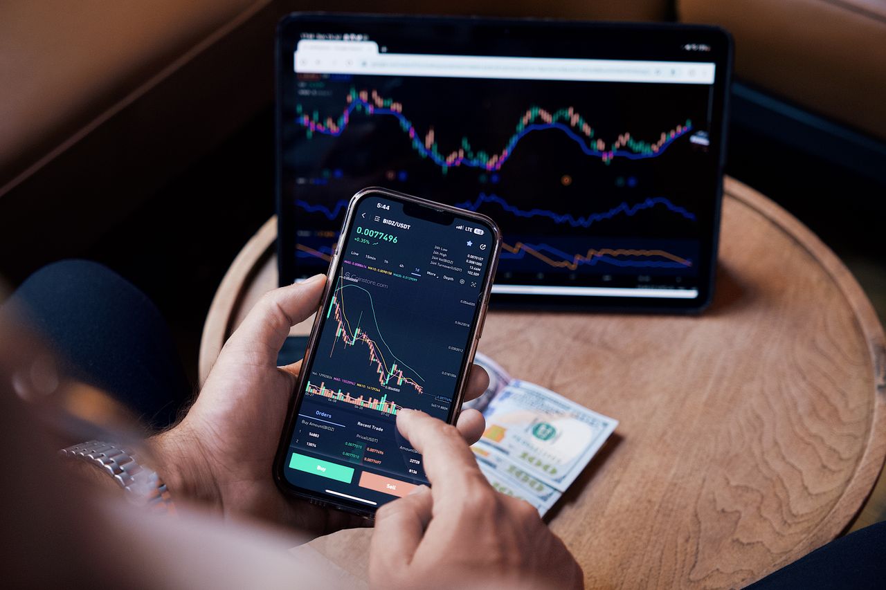 Close-up view of someone buying and selling stocks on a smartphone and tablet.